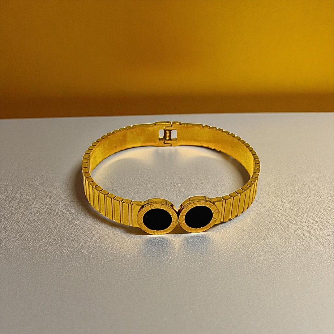 Gold Bracelet for Women with black stones on a gray surface and yellow background