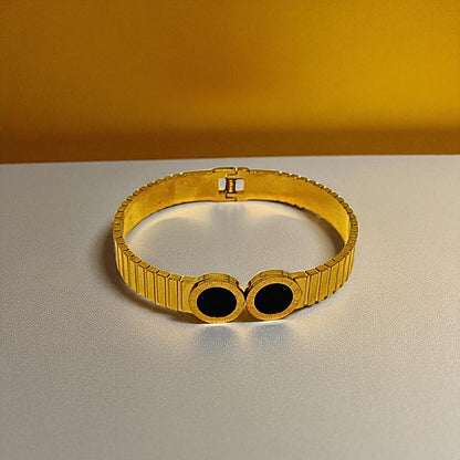 Gold Bracelet for Women with black stones on a gray surface and yellow background