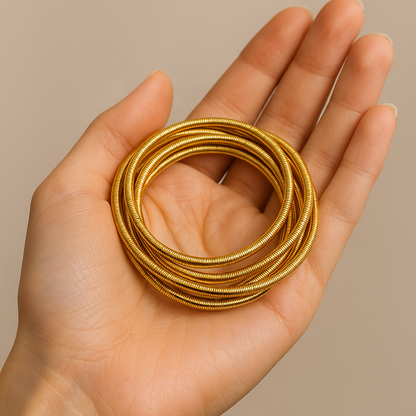 Hand holding a stack of gold Bracelet for Women against a beige background