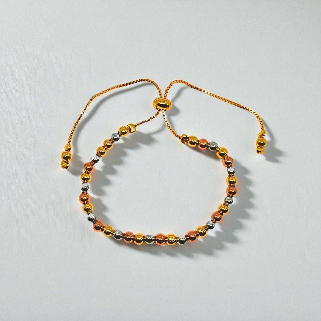 Gold beaded bracelet for Women held in a hand against a beige background