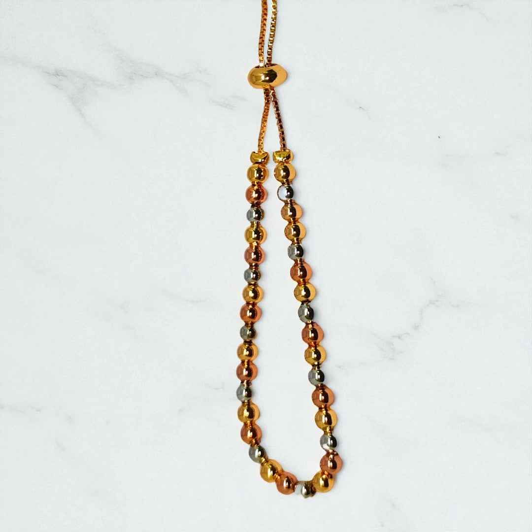 Gold beaded bracelet for Women held in a hand against a beige background
