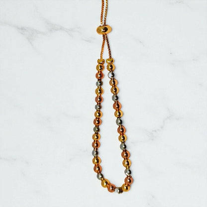Gold beaded bracelet for Women held in a hand against a beige background