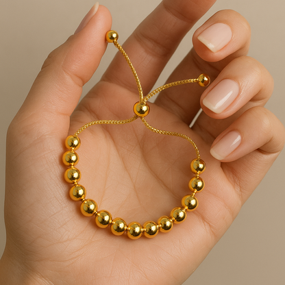 Gold beaded bracelet for Women held in a hand against a beige background