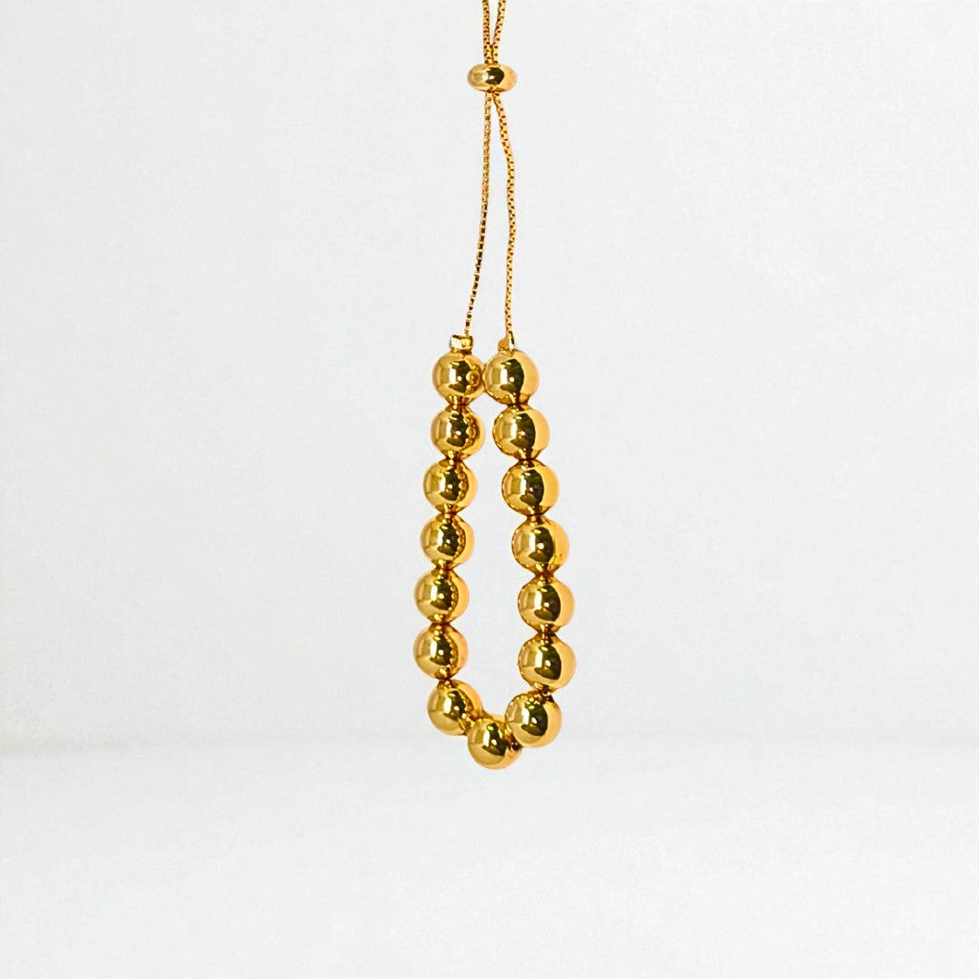 Gold beaded bracelet for Women held in a hand against a beige background