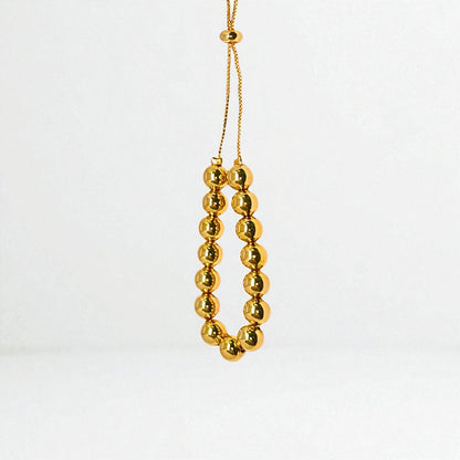 Gold beaded bracelet for Women held in a hand against a beige background