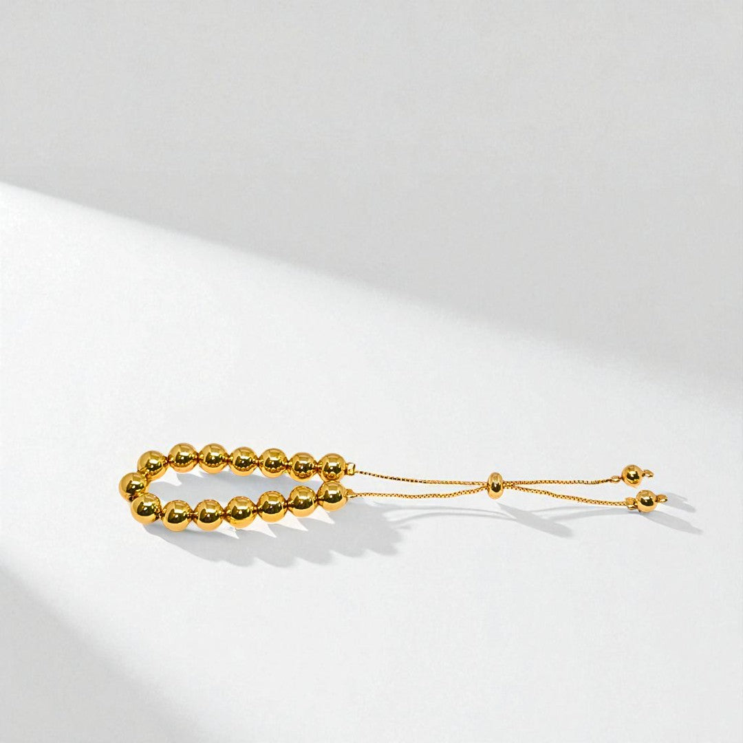 Gold beaded bracelet for Women held in a hand against a beige background