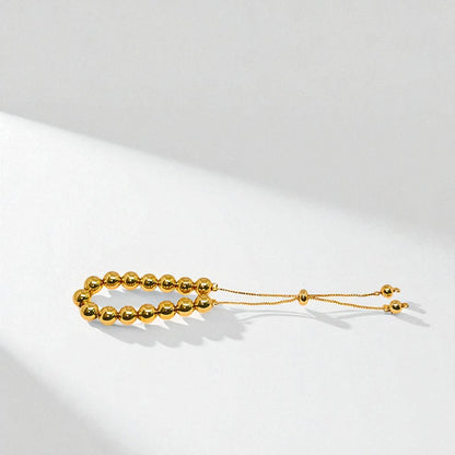 Gold beaded bracelet for Women held in a hand against a beige background