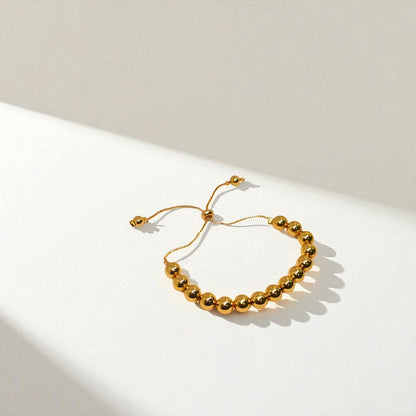Gold beaded bracelet for Women held in a hand against a beige background