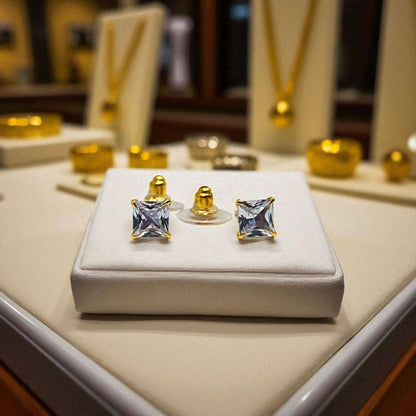 Gold square-cut gemstone earrings for women on a white display box with blurred jewelry store background.