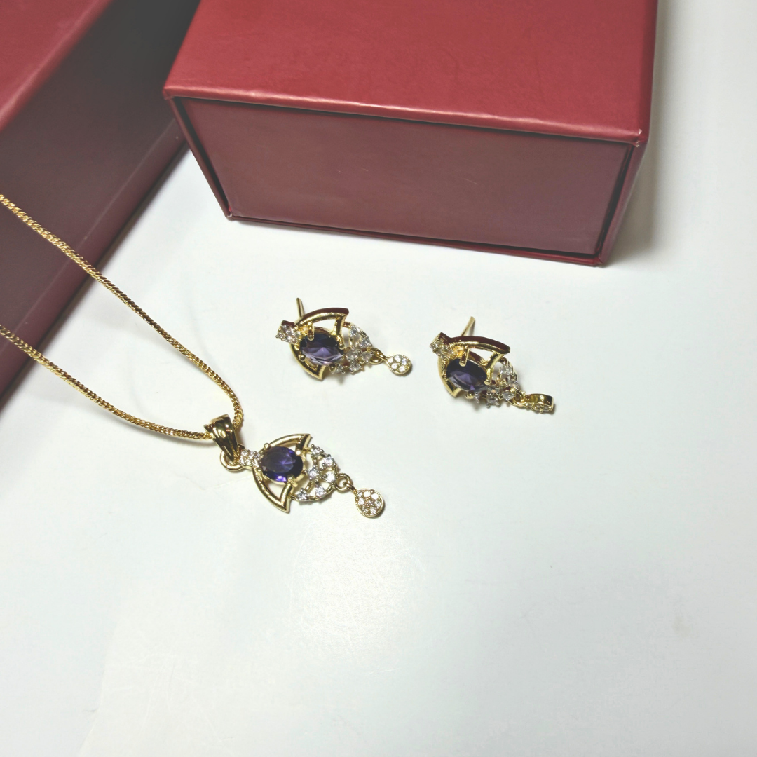 Gold necklace and earrings with purple gemstones on a white surface, next to a red jewelry box.