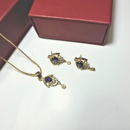 Gold necklace and earrings with purple gemstones on a white surface, next to a red jewelry box.