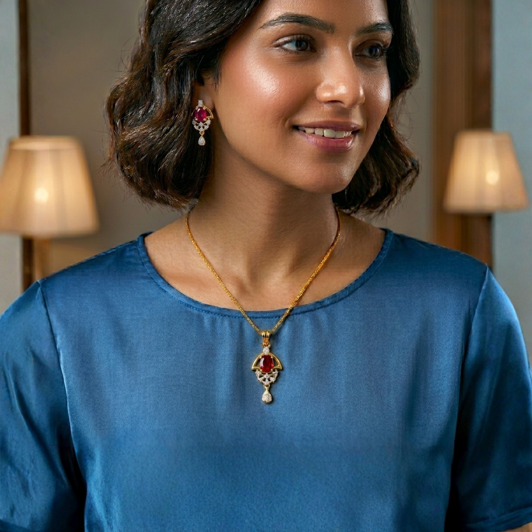 Woman wearing a gold necklace with a red pendant and matching earrings indoors.