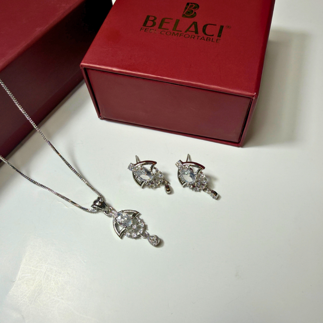 Silver jewelry set with necklace and earrings on a white surface, next to a red Belaci box.