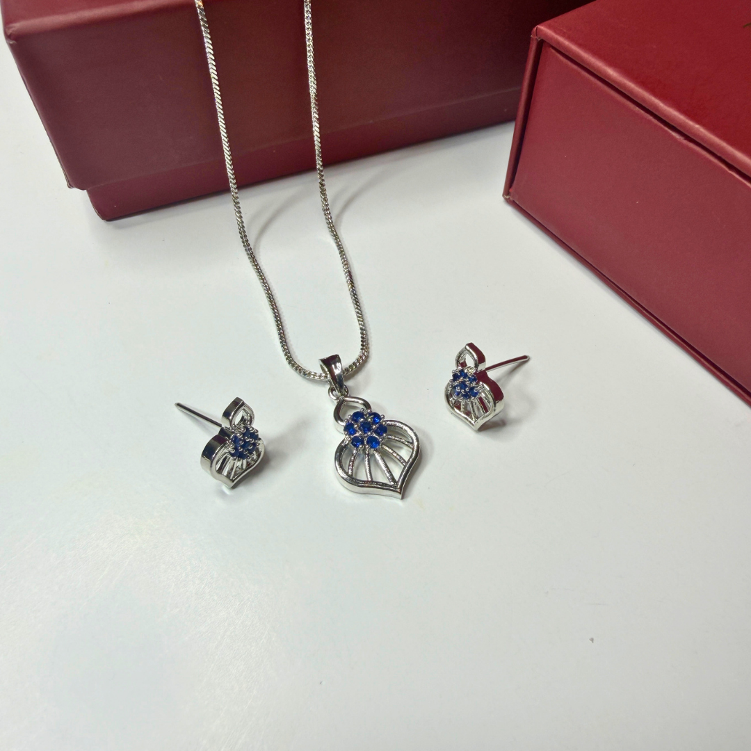 Silver jewelry set with heart-shaped pendants on a white surface with red jewelry box in the background.