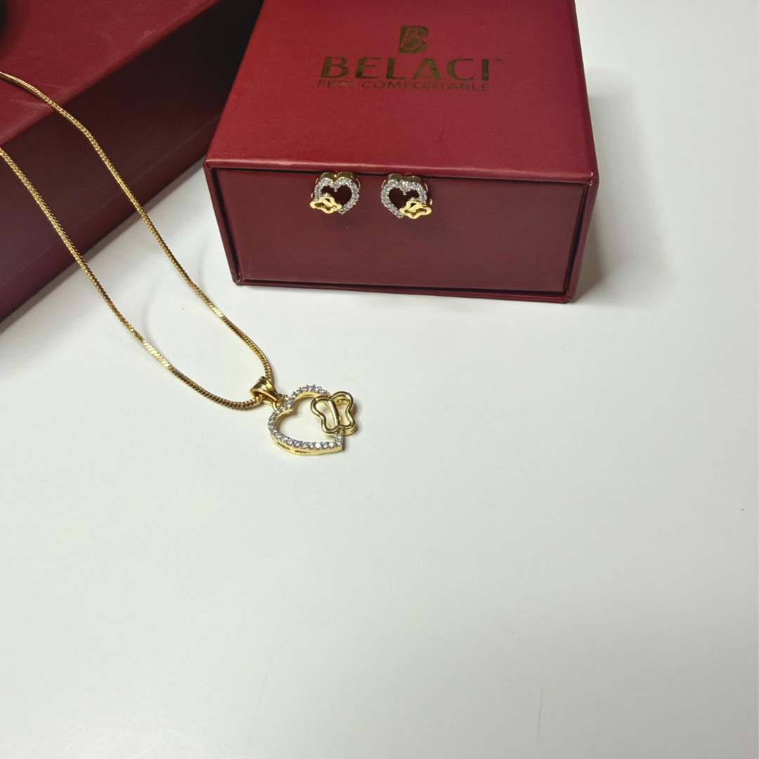 Gold heart-shaped necklace and earrings on a white surface with a red Belaci box in the background.