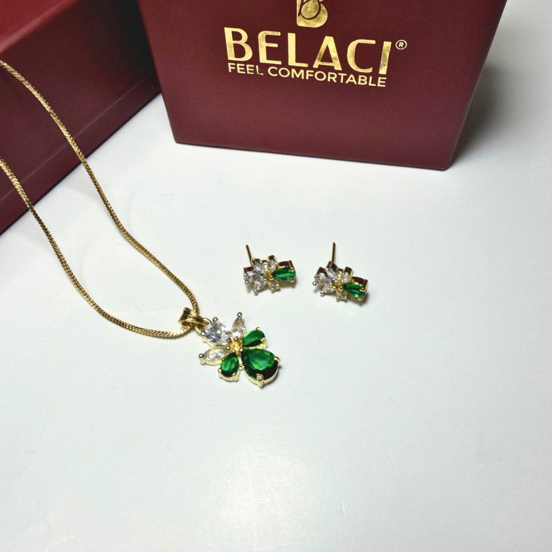 Jewelry set with green gemstones and gold necklace on a white surface with BELACI box in the background.