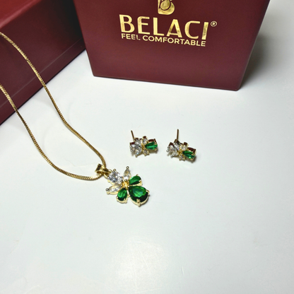 Jewelry set with green gemstones and gold necklace on a white surface with BELACI box in the background.