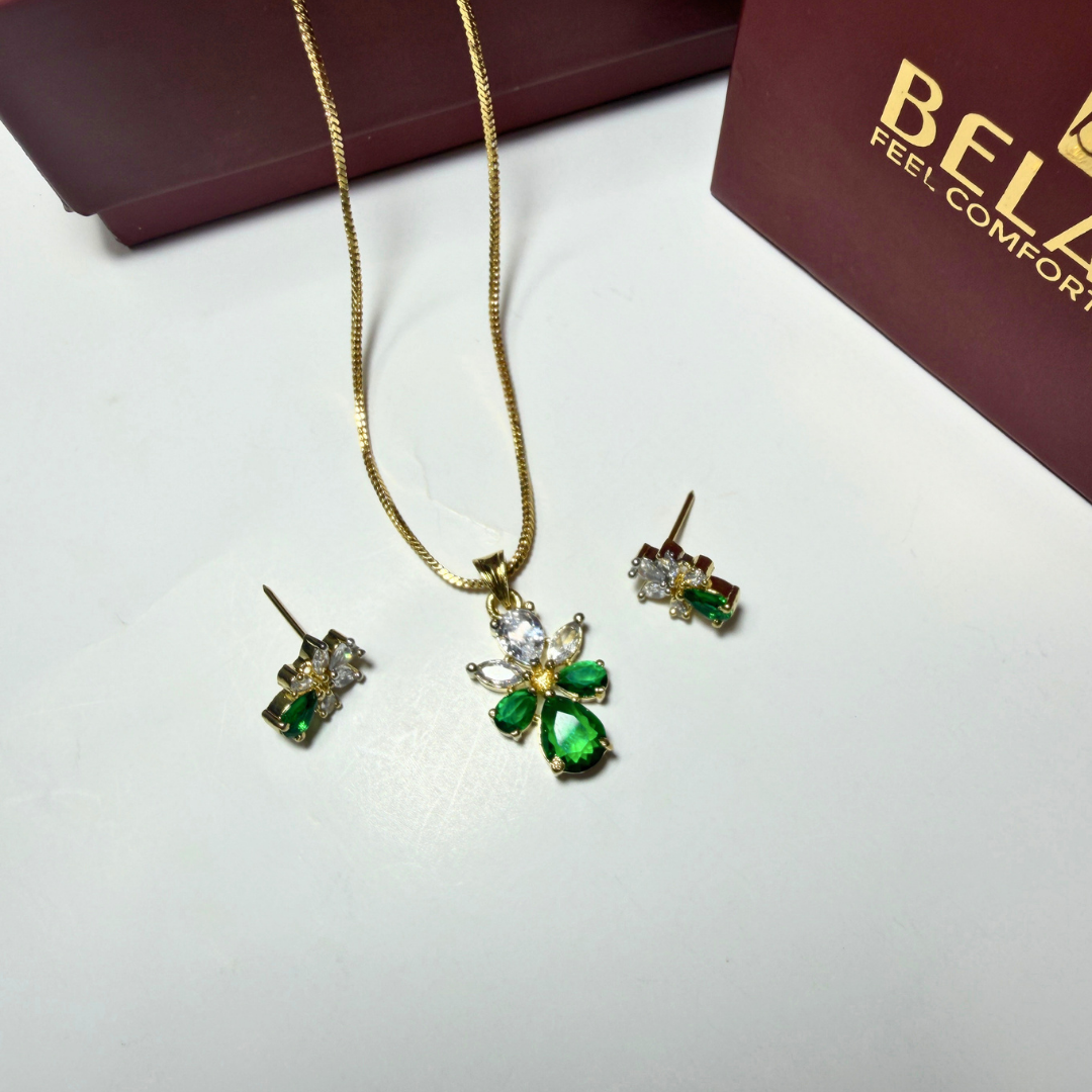 Jewelry set with green gemstones on a white surface with a Belk box in the background.