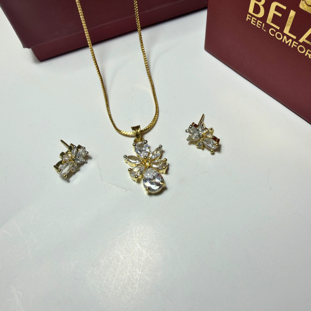 Gold necklace and earrings set on a white surface with a Beladora box in the background.