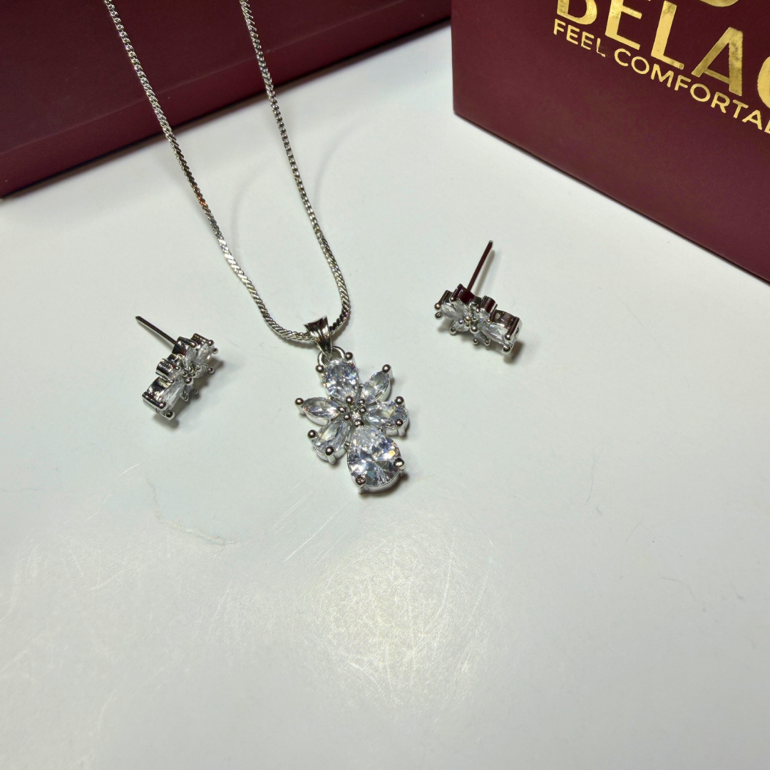 Silver jewelry set with necklace and earrings on a white surface, Beladora box in the background.