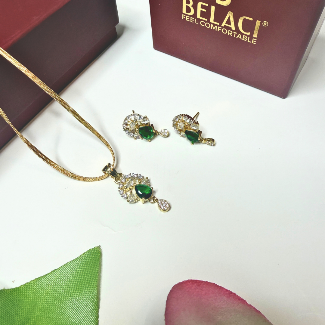 Gold necklace and earrings with green gemstones on a white surface, Belaci brand visible.