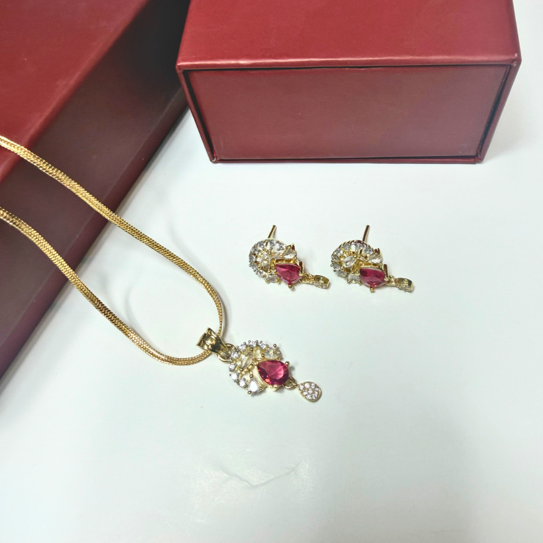 Gold necklace and earrings with red gemstones on a white surface, next to a red jewelry box.