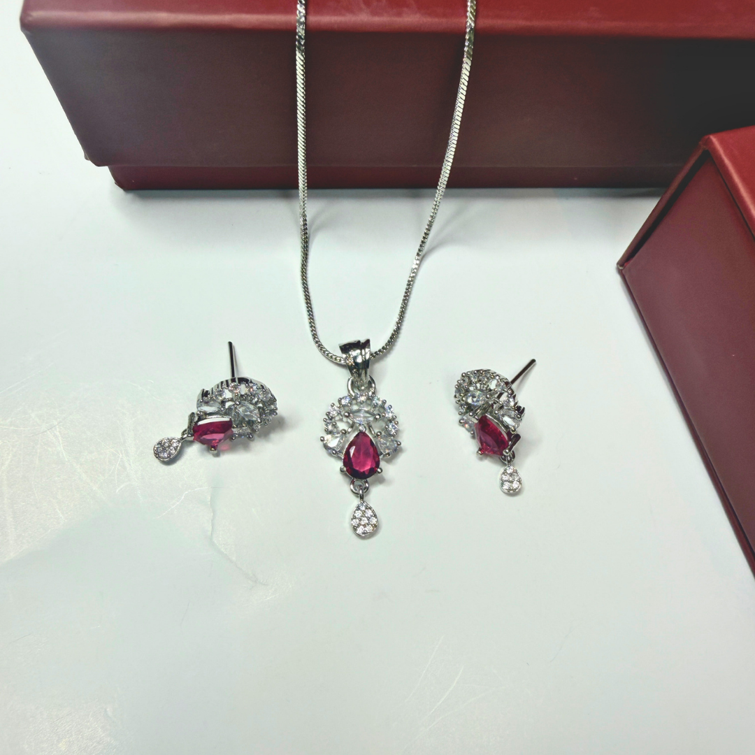 Jewelry set with red gemstones and silver chains on a white surface.