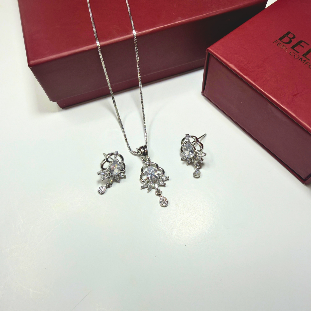 Silver jewelry set with necklace and earrings on a white surface, next to a red box.