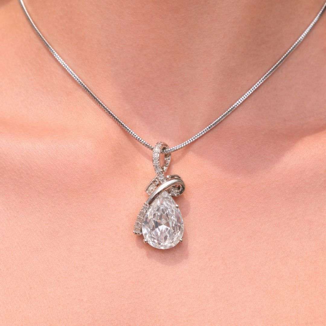 Teardrop-shaped diamond pendant on a silver chain against a soft pink background