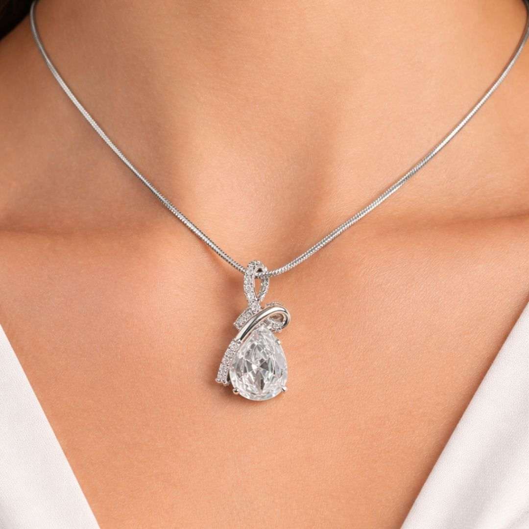 Silver necklace with a pear-shaped diamond pendant on a person wearing a white top.
