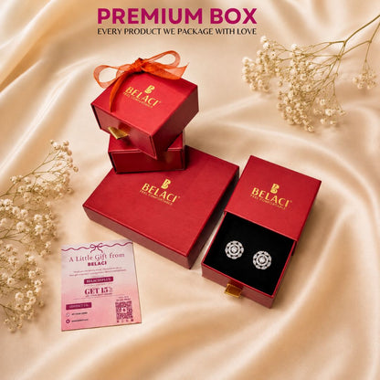 BELACI jewelry gift packaging set on draped champagne satin fabric, featuring red branded boxes, an open box with a pair of silver-toned stud earrings, a gift card, and decorative baby's breath flowers.