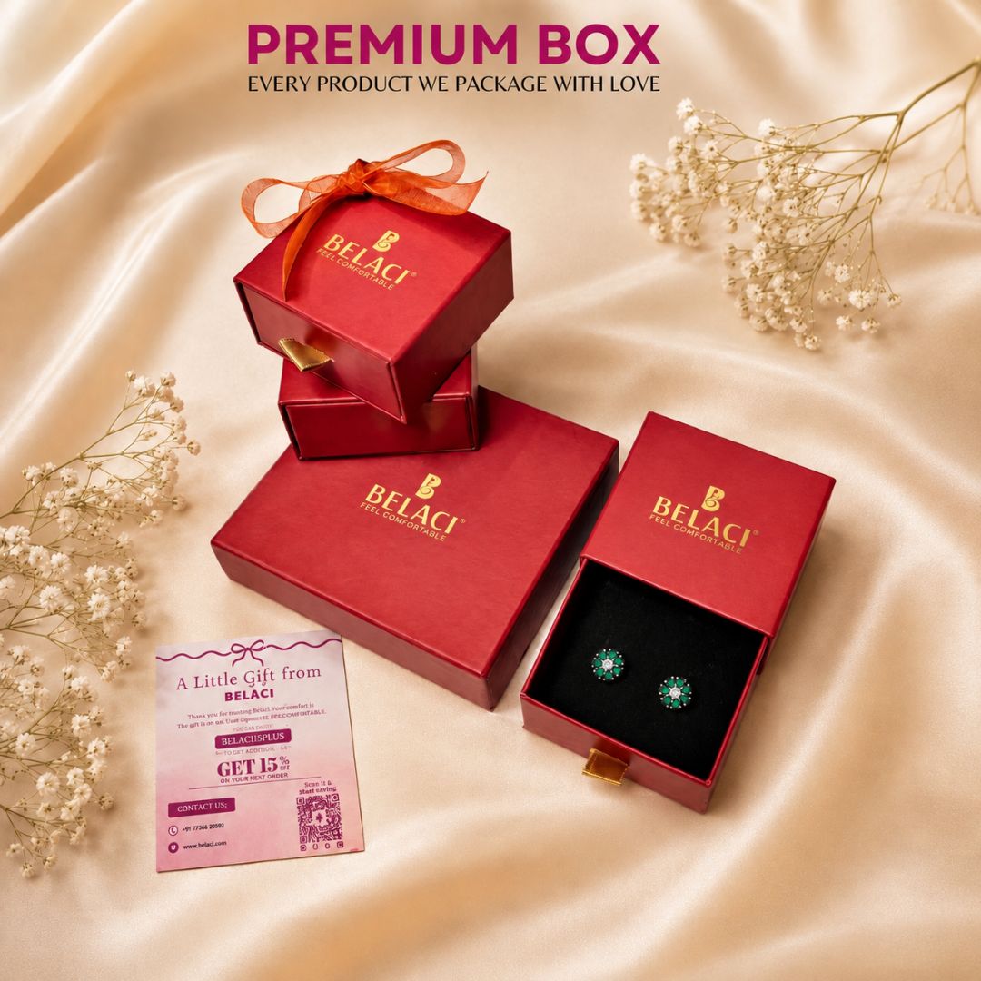 BELACI premium gift packaging set on a beige satin background, featuring red boxes, a pink gift card, and an open box displaying green gemstone stud earrings.