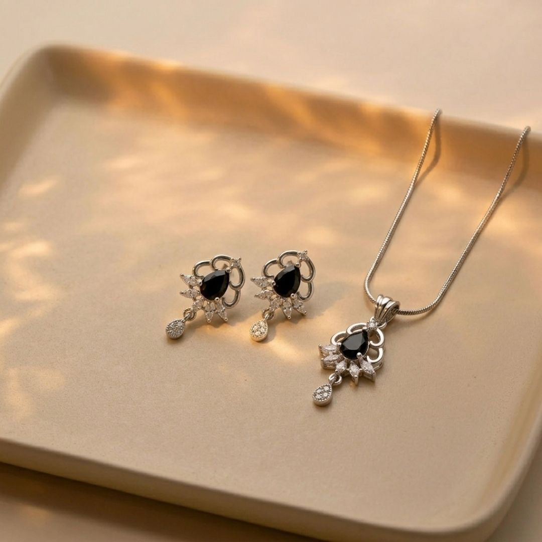 Silver necklace and earring set with black teardrop stones and clear crystals on a beige tray