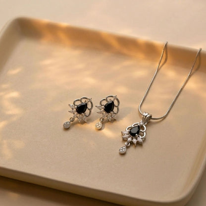 Silver necklace and earring set with black teardrop stones and clear crystals on a beige tray