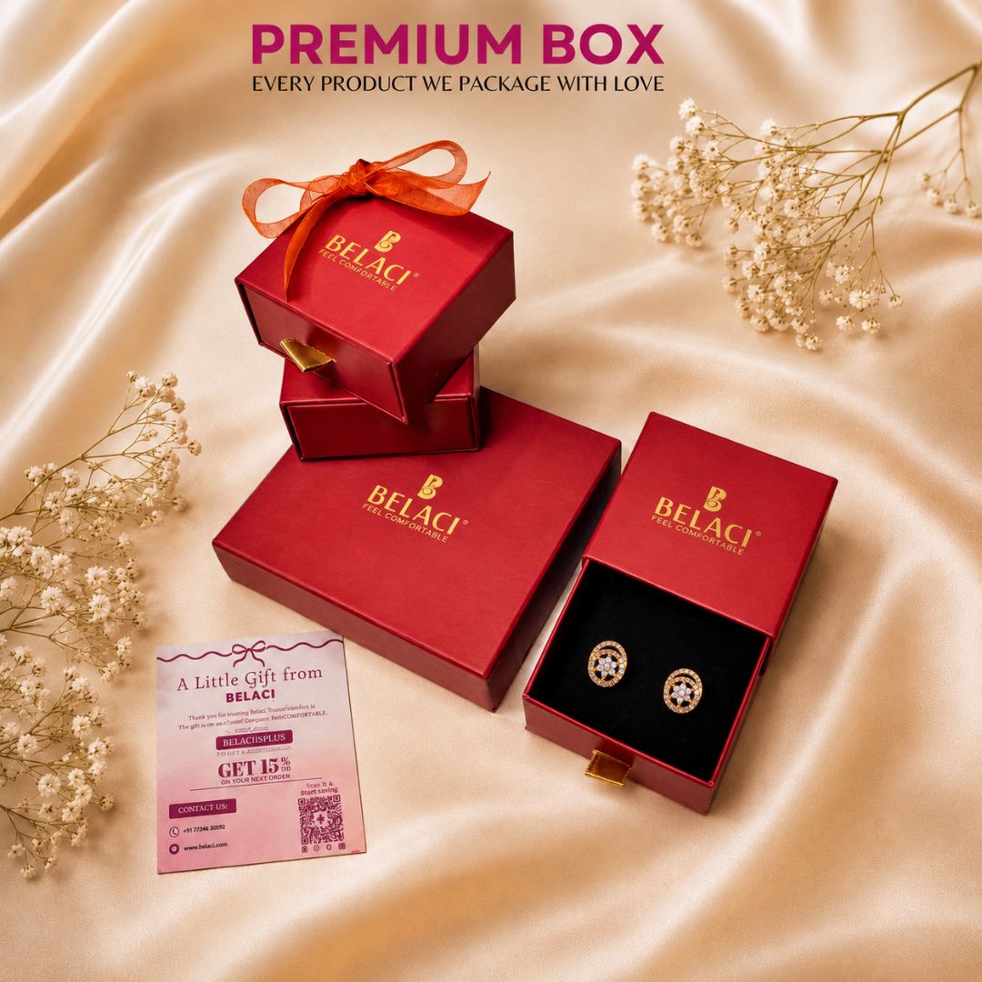 BELACI jewelry gift packaging set on a champagne satin background with dried baby's breath flowers. The set includes a red gift box with an orange ribbon, a red box with the BELACI logo, an open red box showing a black jewelry insert with round earrings, and a pink promotional card.