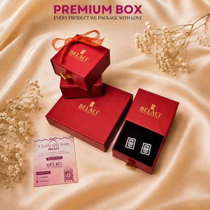 Red jewelry gift boxes with Belaci logo and a pair of rectangular diamond stud earrings on a beige silk background
