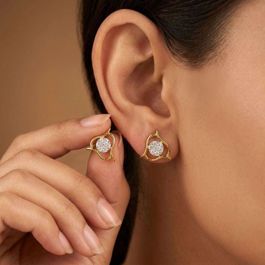 Gold earrings with heart-shaped designs worn by a person against a warm-toned background