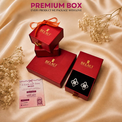 Red jewelry boxes with Belaci branding and diamond stud earrings on a gold satin background