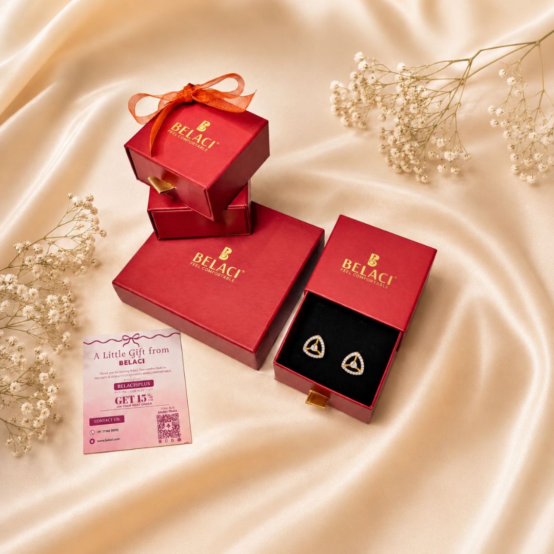Belaci brand red gift boxes and an open box displaying gold heart-shaped earrings on a black insert, arranged on a beige satin fabric with baby's breath flowers and a gift card.