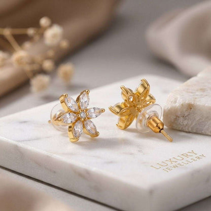 Gold floral earrings on a marble surface with 'Luxury Jewellery' branding.