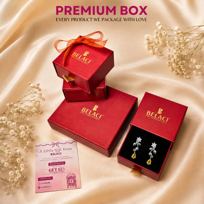 BELACI premium jewelry gift box set arranged on draped champagne satin fabric with baby's breath flowers. The set includes multiple red gift boxes, one open box displaying gold and white floral earrings on a black insert, and a pink gift card.