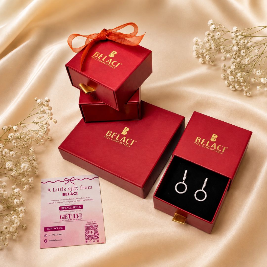 Red jewelry boxes with Belaci logo and silver circle earrings on a satin background with baby breath flowers