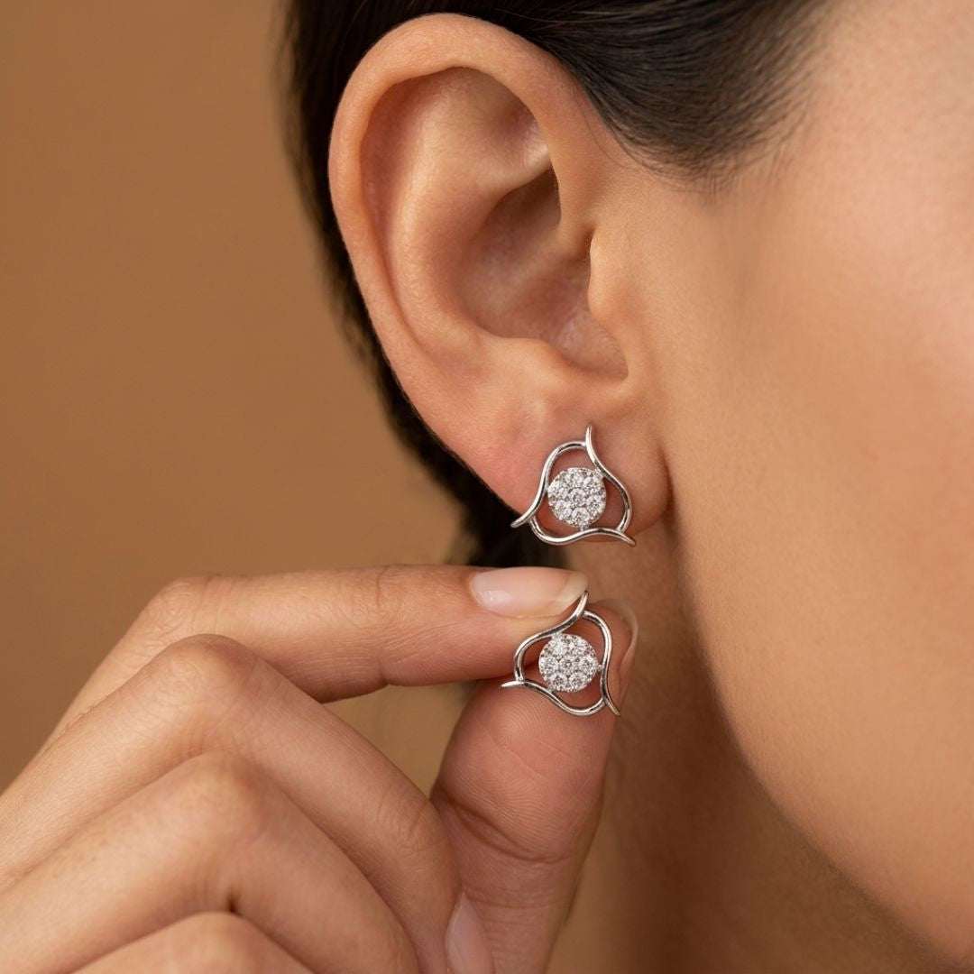 Close-up of a woman wearing silver earrings with clear gemstones against a brown background