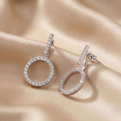 Silver hoop earrings with clear stones on a beige fabric background