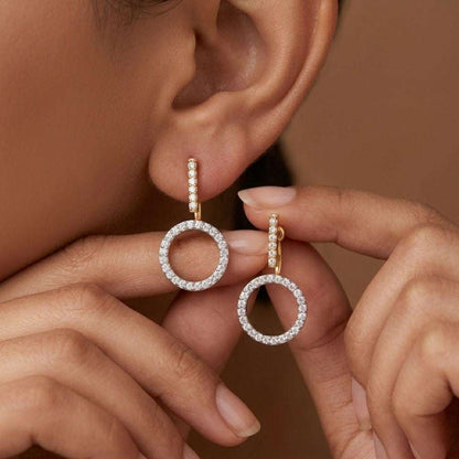 Close-up of a person wearing gold hoop earrings with clear stones against a neutral background