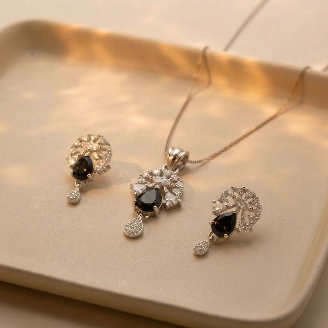 Silver jewelry set with black teardrop stones and clear crystals on a beige tray