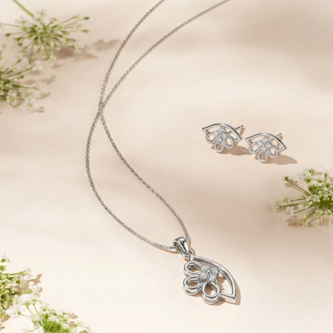 Silver necklace and matching stud earrings with floral diamond accents on a cream background with white flowers