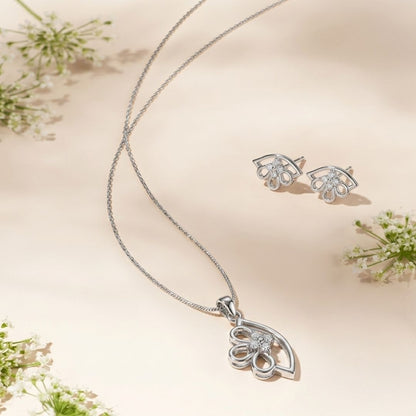 Silver necklace and matching stud earrings with floral diamond accents on a cream background with white flowers