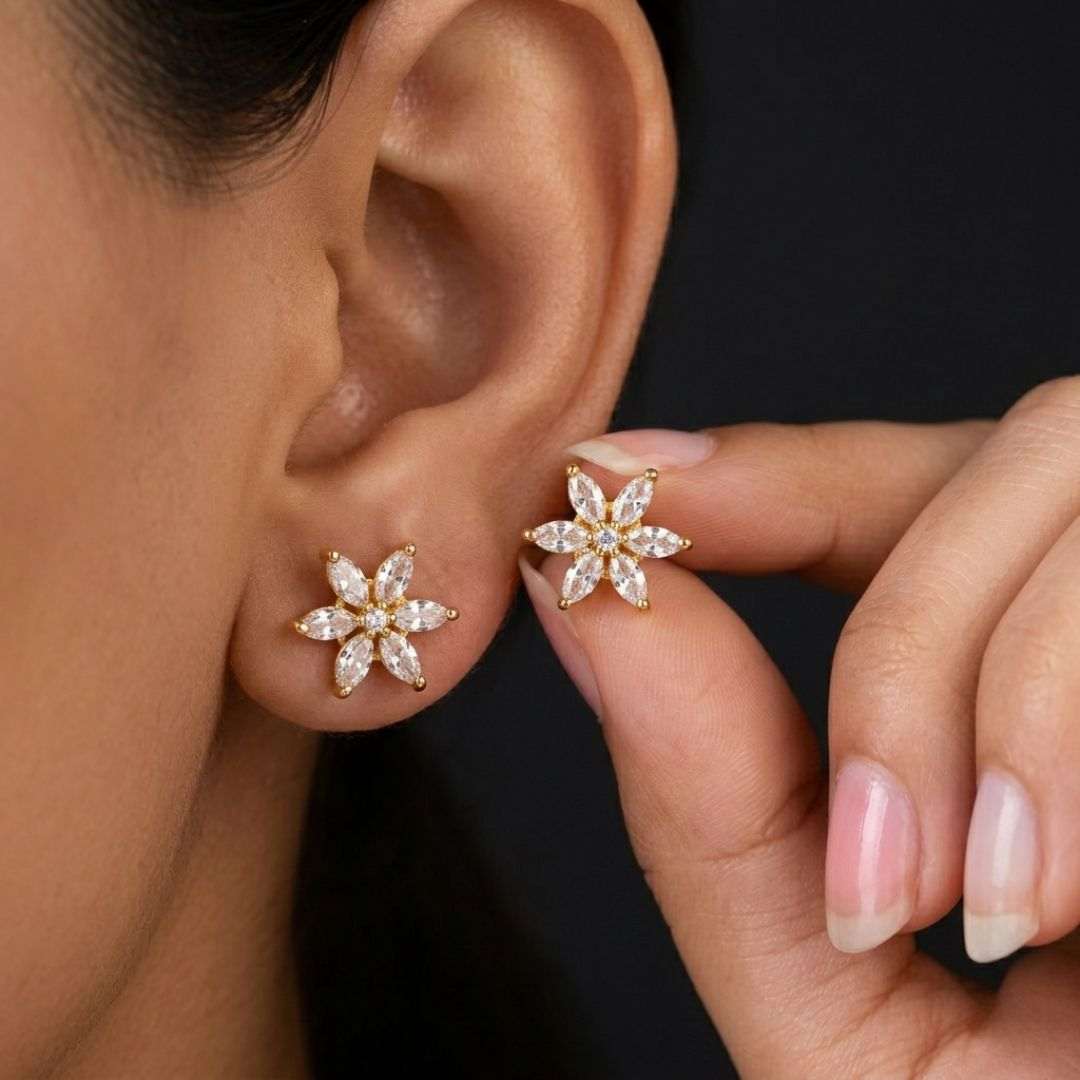 Close-up of a person wearing gold flower-shaped earrings with clear stones.