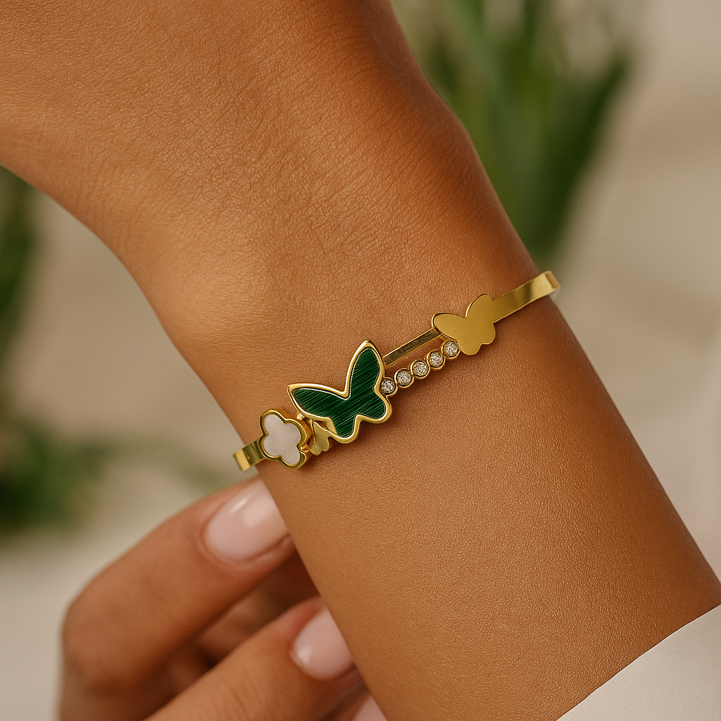 Gold Bracelet for Women with butterfly and clover charms on a wrist against a blurred background